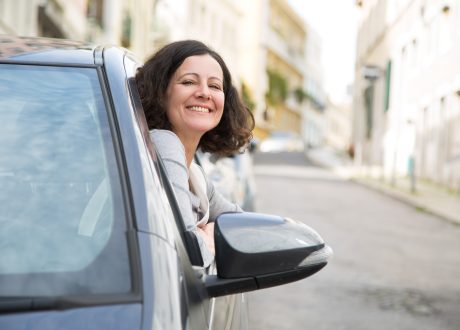 Mulher sentada no carro, no lugar do condutor, com a cabeça fora da janela.