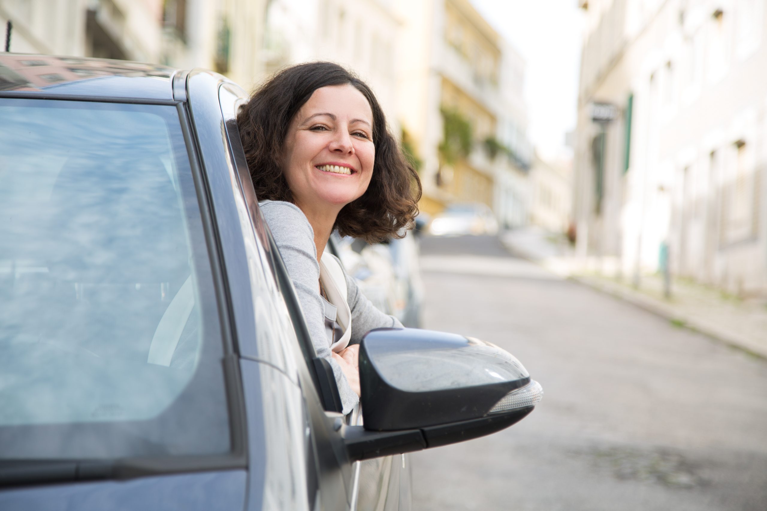 Mulher sentada no carro, no lugar do condutor, com a cabeça fora da janela.